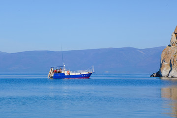 Obraz premium A pleasure tourist boat floats on the water of Lake Baikal. Rocky cape Burhan near the island of Olkhon, Russia.