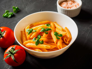 Pasta Penne in tomato sauce Pomodoro, garnished green basil leaves on black table. Traditional italian food