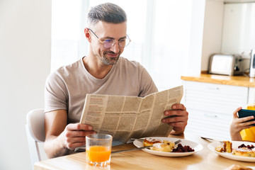 Fototapeta na wymiar Photo of man reading newspaper while having breakfast with his daughter