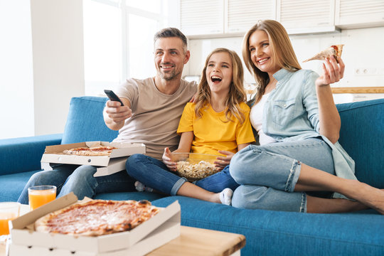 Photo of cheerful family eating popcorn and pizza while watching tv