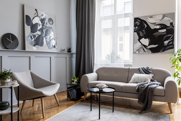 Stylish scandinavian home interior of living room with design gray sofa, armchair, marble stool, black coffee table, modern paintings, decoration, plant and elegant personal accessories in home decor.