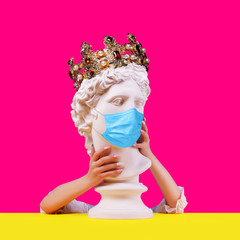 Gypsum statue of Apollo head in crown. Creative. Plaster statue    of Apollo head in medical mask. Woman hands  . On a pink background. Concept art collage.