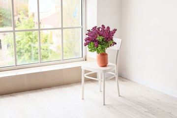 Vase with beautiful lilac flowers on chair in room