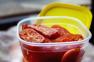 sliced pieces of salami sausage are in a plastic food container with a yellow lid, perfect for a quick snack on the road or to work