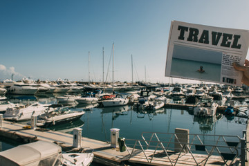 cropped view of woman holding travel newspaper near docked ships in mediterranean sea