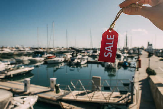 cropped view of woman holding red tag with sale lettering near docked yachts in mediterranean sea
