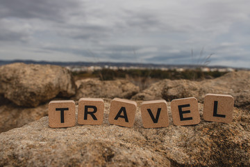 wooden cubes with travel lettering on stones against sky