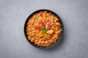 Ful Medames or Fava Beans in black bowl at grey backdrop. Foul Mudammas is a Egyptian, Lebanese, Syrian, Eritrean, Israeli cuisines breakfast dish of cooked beans with cumin, tomatoes, parsley