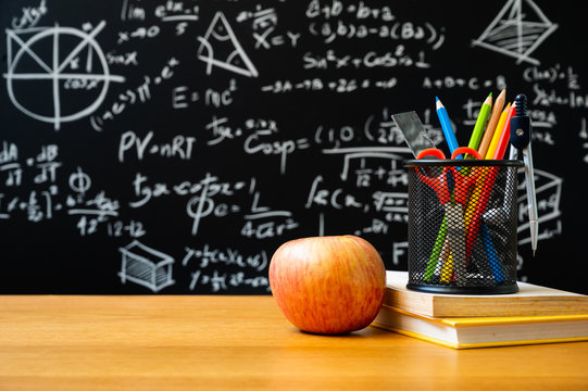 Education background concept. Stationery in holder color pencil, compasses tool, scissors, rulers, sharpener with apple On chalkboard with the Mathematical formula.