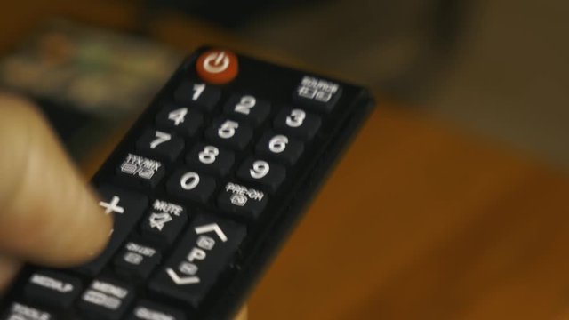 Dedo pulgar de mano izquierda pulsando tecla volumen en control remoto de televisor.