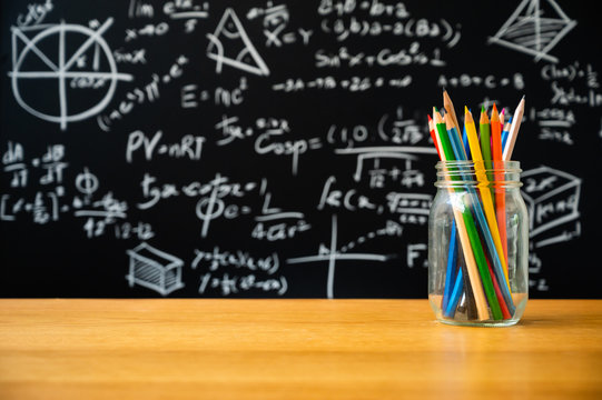 Education background concept. Stationery in glass jar color pencil, compasses tool, scissors, rulers, sharpener On chalkboard with the Mathematical formula background.