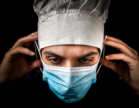 young chef wears health mask due to emergency called covid 19 on a black background 