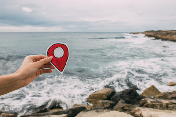 cropped view of woman holding red paper as location sign near mediterranean sea