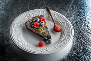 Slice of chocolate cake with nuts, decorated with berries, blueberries and raspberries.