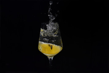 Studio shot with freeze motion of lemon slice splashing into the glass full of water- isolated on black background