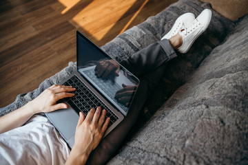 Handsome man is using a laptop while lying on sofa in living room with long legs and white...