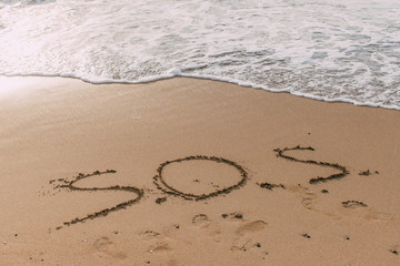 summer beach with sos lettering on sand near sea