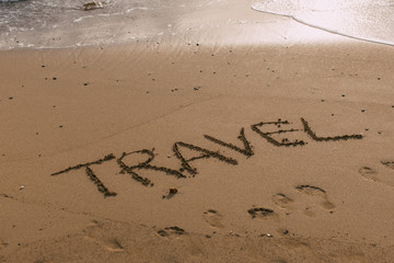 beach with travel lettering on sand near sea