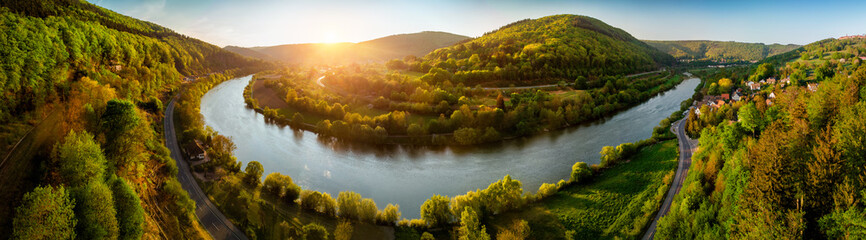 Panoramic aerial landscape shot of Neckar river, Germany, at a beautiful sunset, with clear sky and the vegetation being colorfully lit, a road following alongside the water