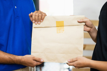 Close up hands accepting a delivery of paper bag from deliveryman. Image of Delivery, Courier, Service, Shipment, Import Export Concept.