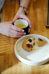 tasty and delicious nut cookies in a white plate and woman's hands holding a cup of green tea