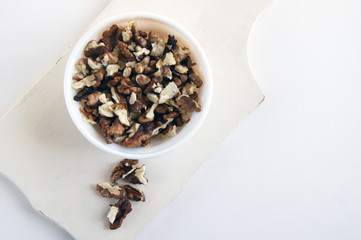 Peeled walnuts in a white cup on a wooden board on a white background.