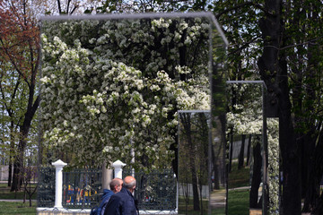 two men reflected in a big mirrors outdoors in the city park in the springtime