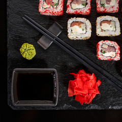 Japanese restaurant, sushi roll on black slate. Set with chopsticks, ginger and wasabi on a dark background.