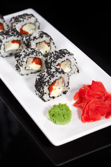 Japanese Traditional Cuisine. A roll of sushi with sesame is served on a white plate, decorated with wasabi and ginger.