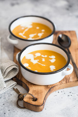 Pumpkin cream soup. Roasted pumpkin and carrot puree soup with turmeric, cream, paprica, chives and pumpkin seeds on grey background. Vegetarian cousine. Vegan recipe. Green living.