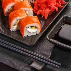 Sushi with chopsticks, ginger and soy sauce in a black bowl on a stone board. Japanese food.
