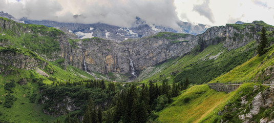 Dramatic panoramic view of a valley in the swiss alps with clouds, forest and waterfalls at Klausenpass at Canton Uri in Switzerland