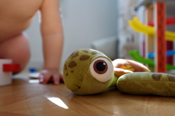 Baby toddler in diaper playing with a plush sea turtle in his bedroom on a sunny day.