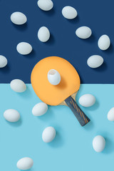 The yellow racket is in the middle of the table. There is a split egg on the racket. There are other eggs lying around. The frame is divided in blue into two parts. Flat lay