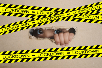 Little girl peeking from a hole on cardboard box with lockdown sign. selective focus on her eye. Concept of lockdown on global crisis