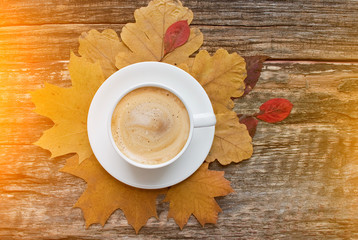 A cup of coffee with cappuccino and autumn leaves on old wooden background. Autumn decor, fall mood, autumn still life.