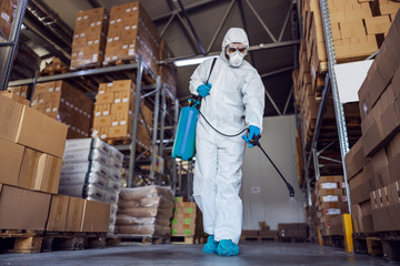 Fototapeta na wymiar Man in protective suit and mask disinfecting warehouse full of food products from corona virus / covid-19.
