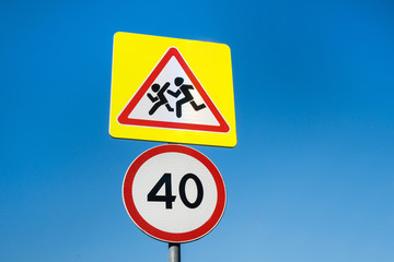 International signs 'Speed limit' (to 40 km/hour, below) & 'Children crossing' (above). Clear blue sky is on background