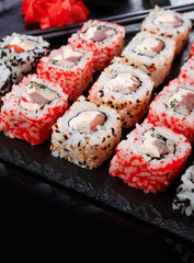 Rolls of sushi uramaki with salmon, smoked eels, cucumber, cream cheese, sesame, avocado and caviar on a black stone board.