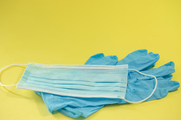 Composition of preventive equipment  against COVID-19 on a yellow background showing blue surgical mask and blue surgical gloves