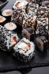 Sushi roll with salmon, eel, cucumber, cream cheese and sesame on a black board.