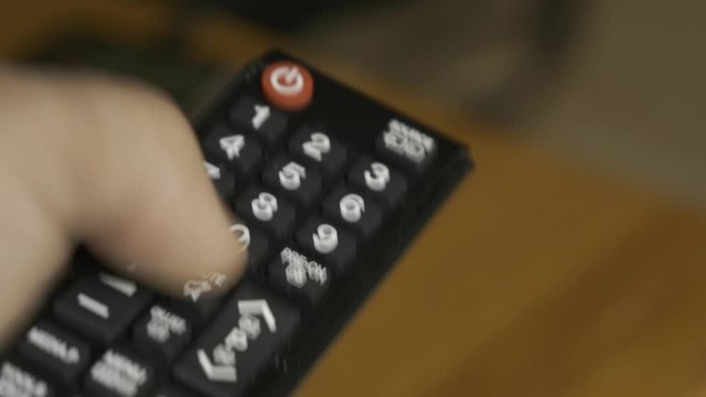 Control remoto de televisor sostenido en mano izquierda. Dedo pulgar pulsando la tecla mute.