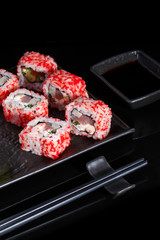Japanese sushi with soy sauce and chopsticks on black background.