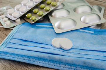 different pills in blister pack and medical mask on a wooden background. Close-up.