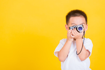 Asian Thai happy portrait cute little cheerful child boy hold photo camera compact photographer doing taking the picture, studio shot isolated on yellow background with copy space