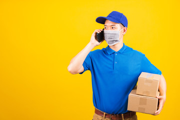 Fototapeta na wymiar Asian young delivery worker man t-shirt and cap uniform wearing face mask protective use smart mobile phone call to customer under coronavirus or COVID-19, studio shot isolated yellow background