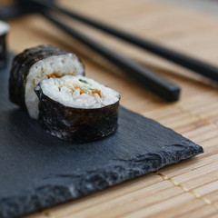 Maki sushi, two pieces of tuna and cucumber on a black board. Black sticks on the background.