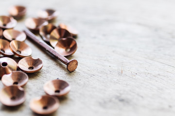 Shiny copper nails and rivets (roves) scattered on a white wooden surface
