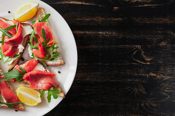Sandwich with salmon, cheese, arugula and lemon on a white plate on a black table