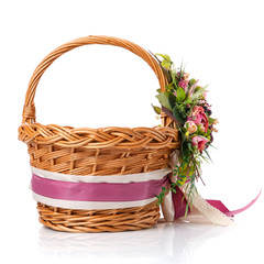 Fototapeta na wymiar Brown wicker basket. Decor with pink flowers, greenery and ribbons. Made for Easter. Side view.